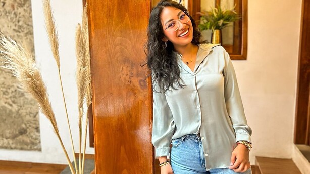 A woman standing in a room with wooden beams, a chandelier, and a window with a plant. - Hotel Boutique Pedregal (Coatepec)