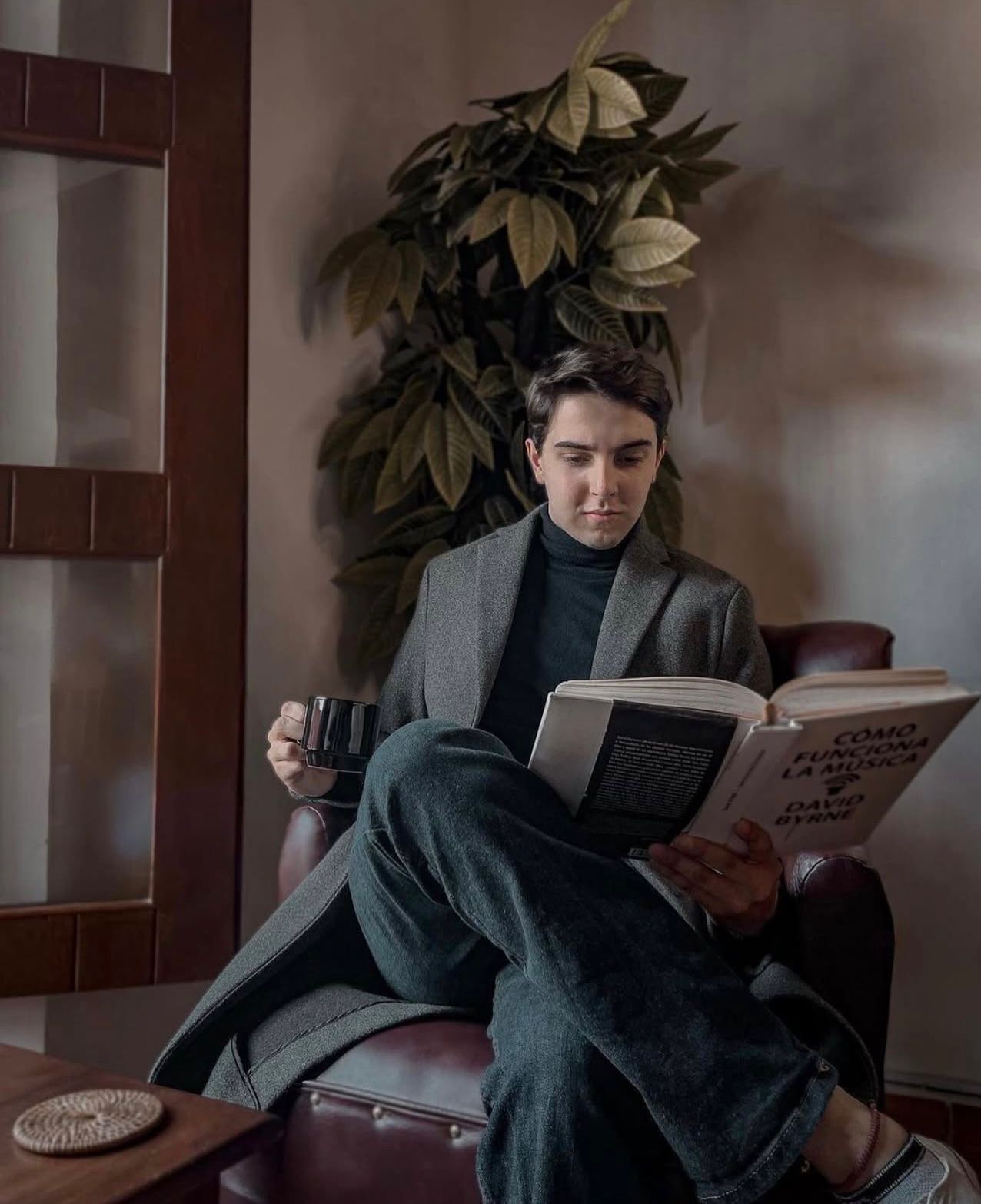 Una persona sentada en un sillón de cuero, sosteniendo un libro titulado 'Como Funciona La Música' de David Byrne.