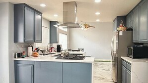 A modern kitchen with grey cabinets, a central island, a stainless steel refrigerator, and a microwave. - Charming 3-bedroom house in Moreno Valley with huge pool ,spa and connected lake (Moreno Valley)