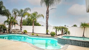 A swimming pool with a curved design, surrounded by palm trees and a white fence. - Charming 3-bedroom house in Moreno Valley with huge pool ,spa and connected lake (Moreno Valley)