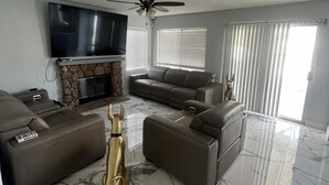 A modern living room with a stone fireplace, leather sofas, a flat-screen TV, and a ceiling fan. - Charming 3-bedroom house in Moreno Valley with huge pool ,spa and connected lake (Moreno Valley)