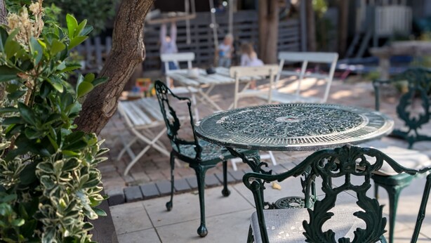 An outdoor seating area with metal tables and chairs, surrounded by greenery and trees. - Cosy Family House | Quiet | Garden | Free Parking (London)