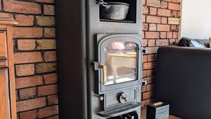 A black wood-burning stove with a glass door, placed against a brick wall. - Cosy Family House | Quiet | Garden | Free Parking (London)