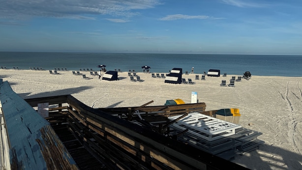 Ein Strand mit Reihen von Liegestühlen und Sonnenschirmen, einer Holzlattenzaun und einem Schild.