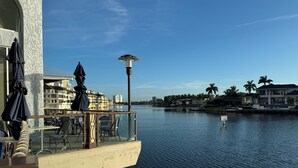 Eine Uferterrasse mit Außenbestuhlung, einer Laterne und Blick auf Wasser und Gebäude.