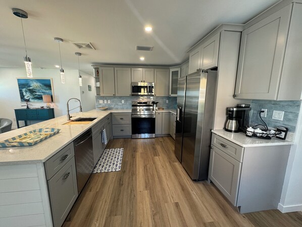 A modern kitchen with grey cabinets, stainless steel appliances, a marble countertop, and a wooden floor.
