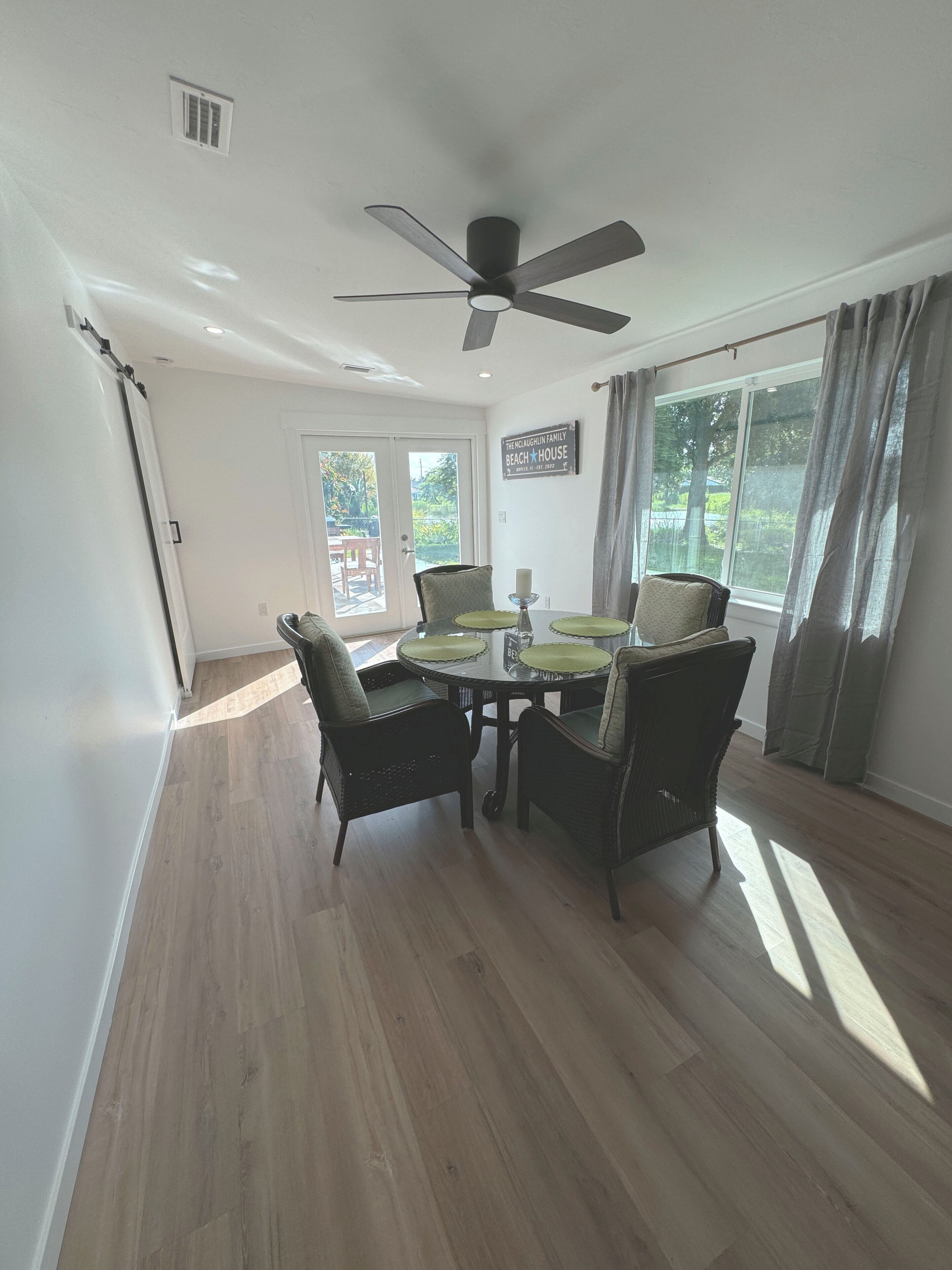 A dining area with a table and four chairs, a ceiling fan, and a window with curtains.