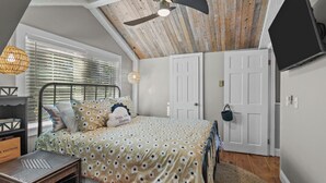 A bedroom with a bed, a ceiling fan, a TV, and a window with blinds.