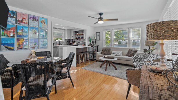 A spacious living area with a dining set, a sofa, and a coffee table. There is a kitchen in the background with a large island.