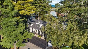A two-story house with a dark roof, surrounded by dense green trees.