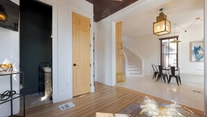 A modern interior with a wooden floor, a staircase, a dining area with chairs, and a hanging light fixture.