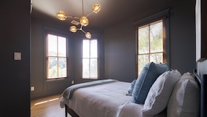 A bedroom with a bed, two windows, a ceiling light fixture, and a wooden floor.