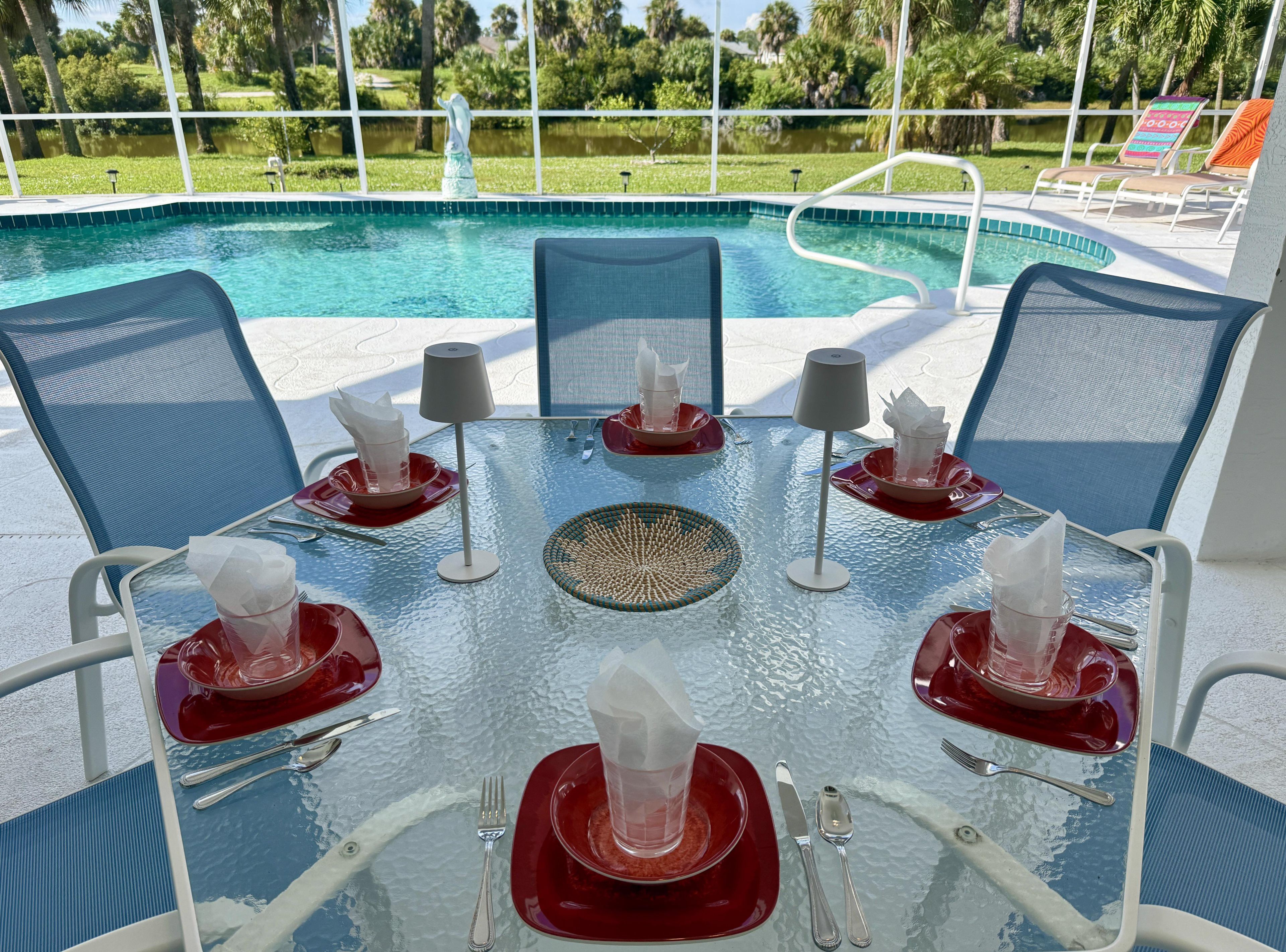Taula de dinar amb superfície de vidre, vaixelles vermelles i cadires, amb vista a una piscina.
