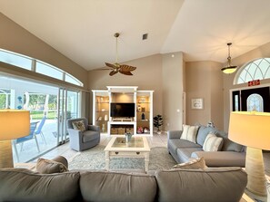 A spacious living room with a large TV, comfortable seating, and a ceiling fan.