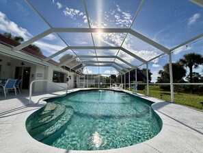 A clear swimming pool with a sunshade structure, surrounded by lounge chairs and a covered patio area.