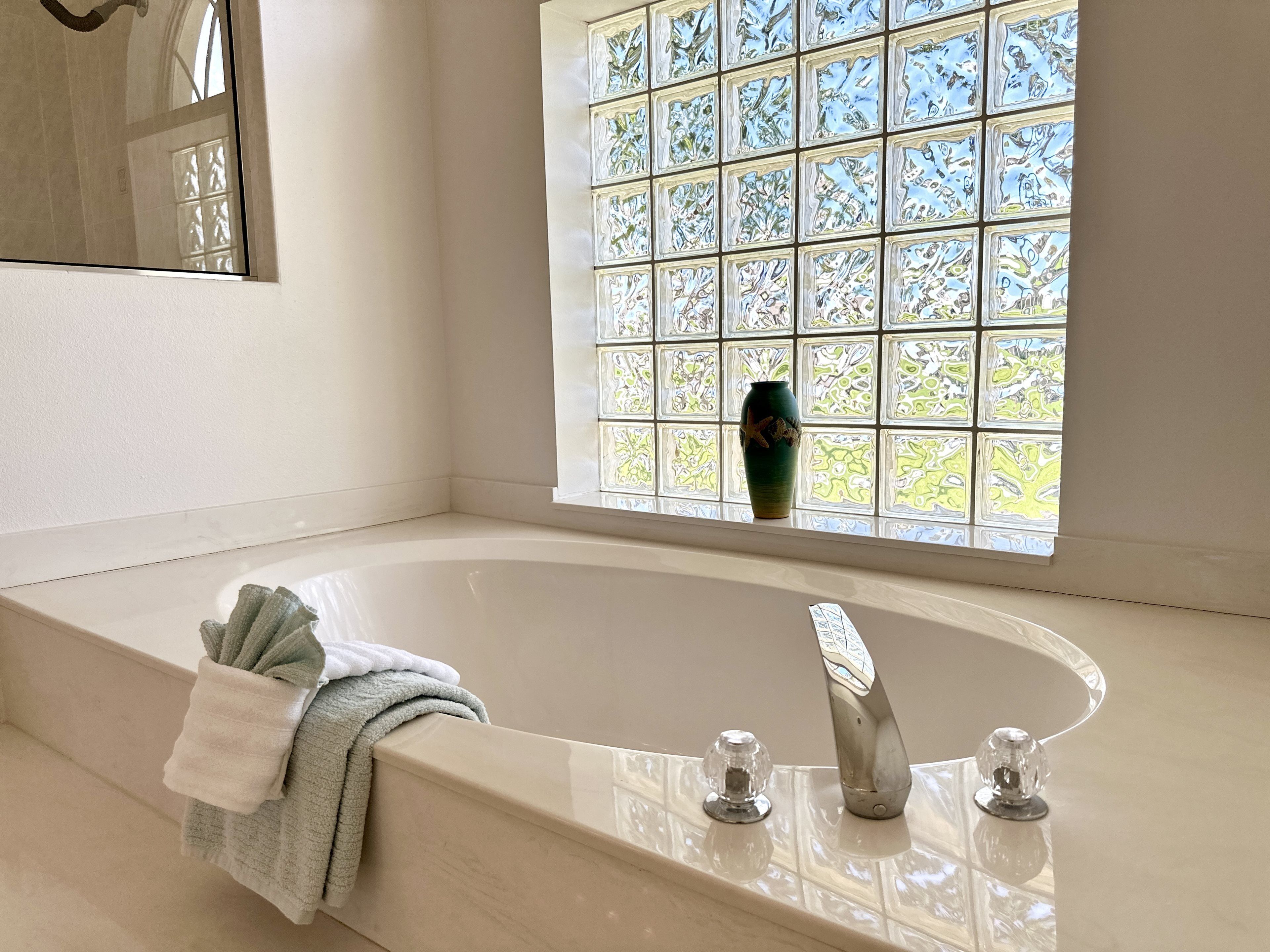 Un baño con una bañera grande, una ventana con vidrio decorativo y un florero en el alféizar.