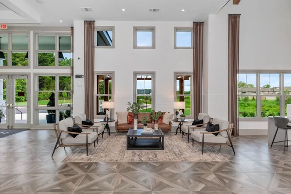 A spacious lobby with a central seating area, large windows, and a view of the outdoors. - Landing Dry Creek Apartments (Huntsville)