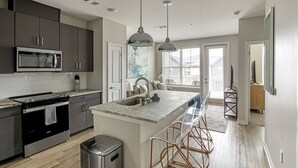 Una cocina moderna con una isla central, electrodomésticos de acero inoxidable e iluminación colgante.