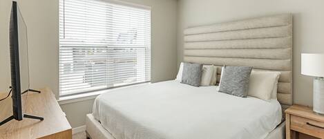 Un dormitorio con cama, mesita de noche, lámpara y ventana con persianas.