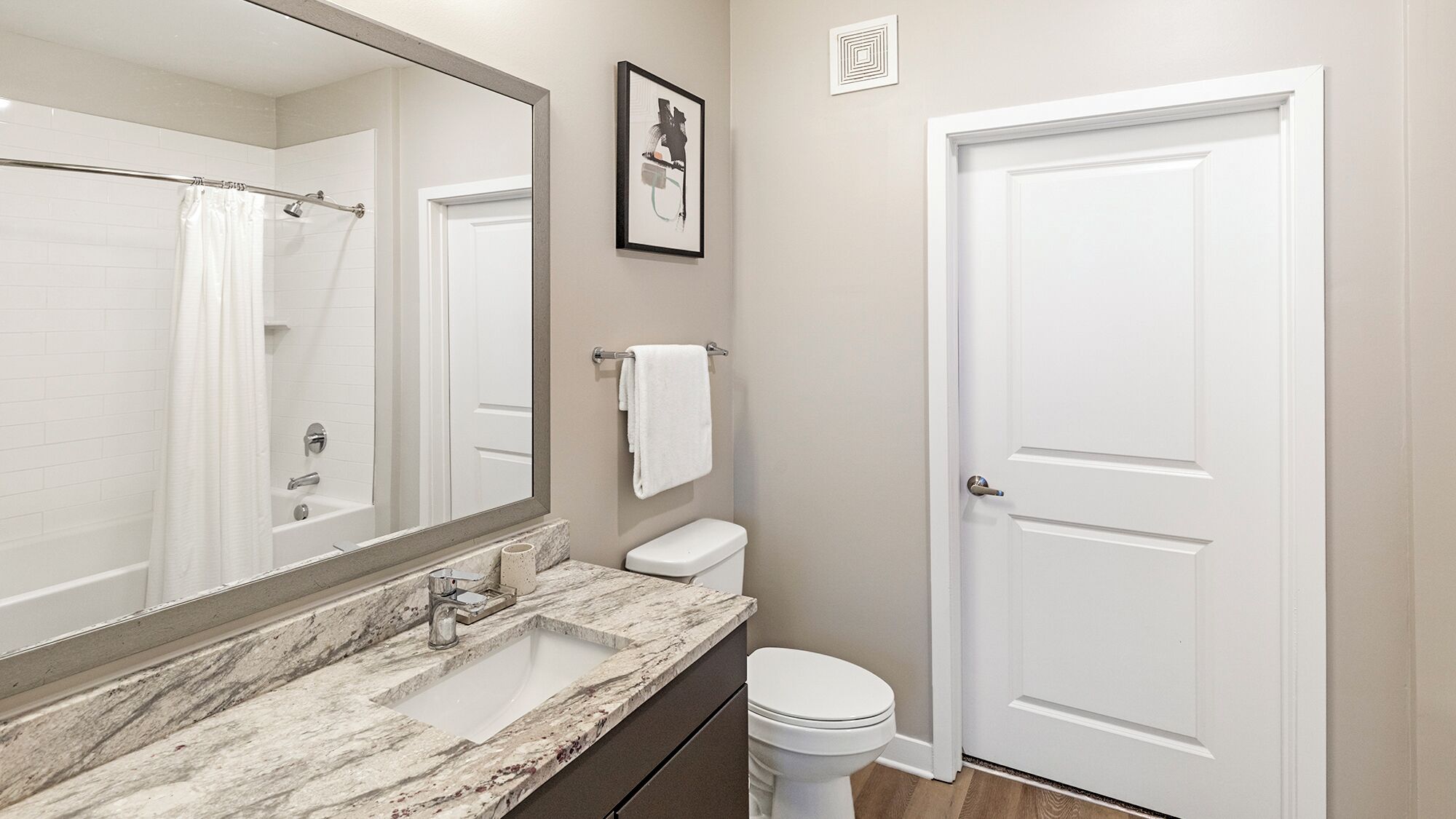 A bathroom with a marble sink, a toilet, a shower curtain, and a framed picture on the wall.