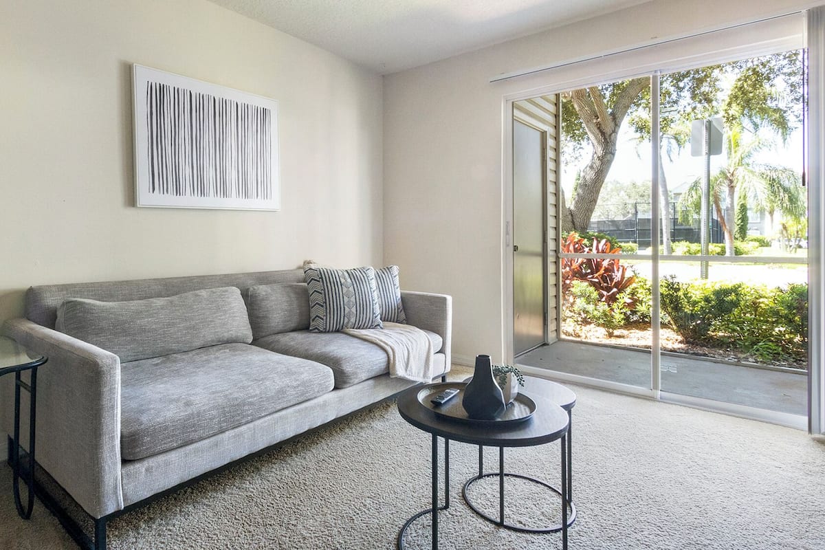 A living room with a grey sofa, a glass coffee table, a lamp, and a painting on the wall.