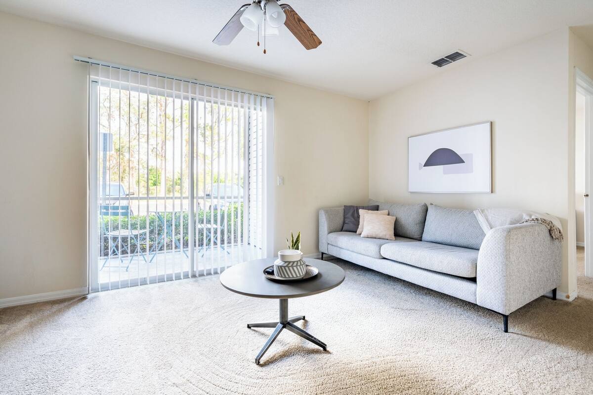 A living room with a grey sofa, a round coffee table, and a ceiling fan.