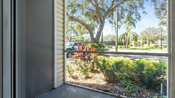 A view from a window with a metal railing, a parking lot, and a variety of trees and shrubs. - Bradenton Apartments by Landing (Bradenton)