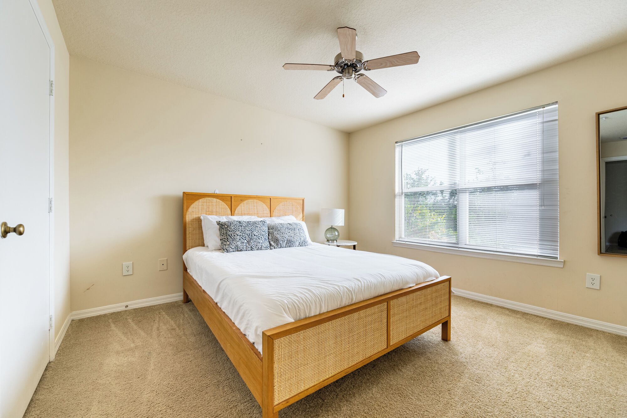 A bedroom with a wooden bed, a ceiling fan, a window with blinds, and a mirror on the wall.