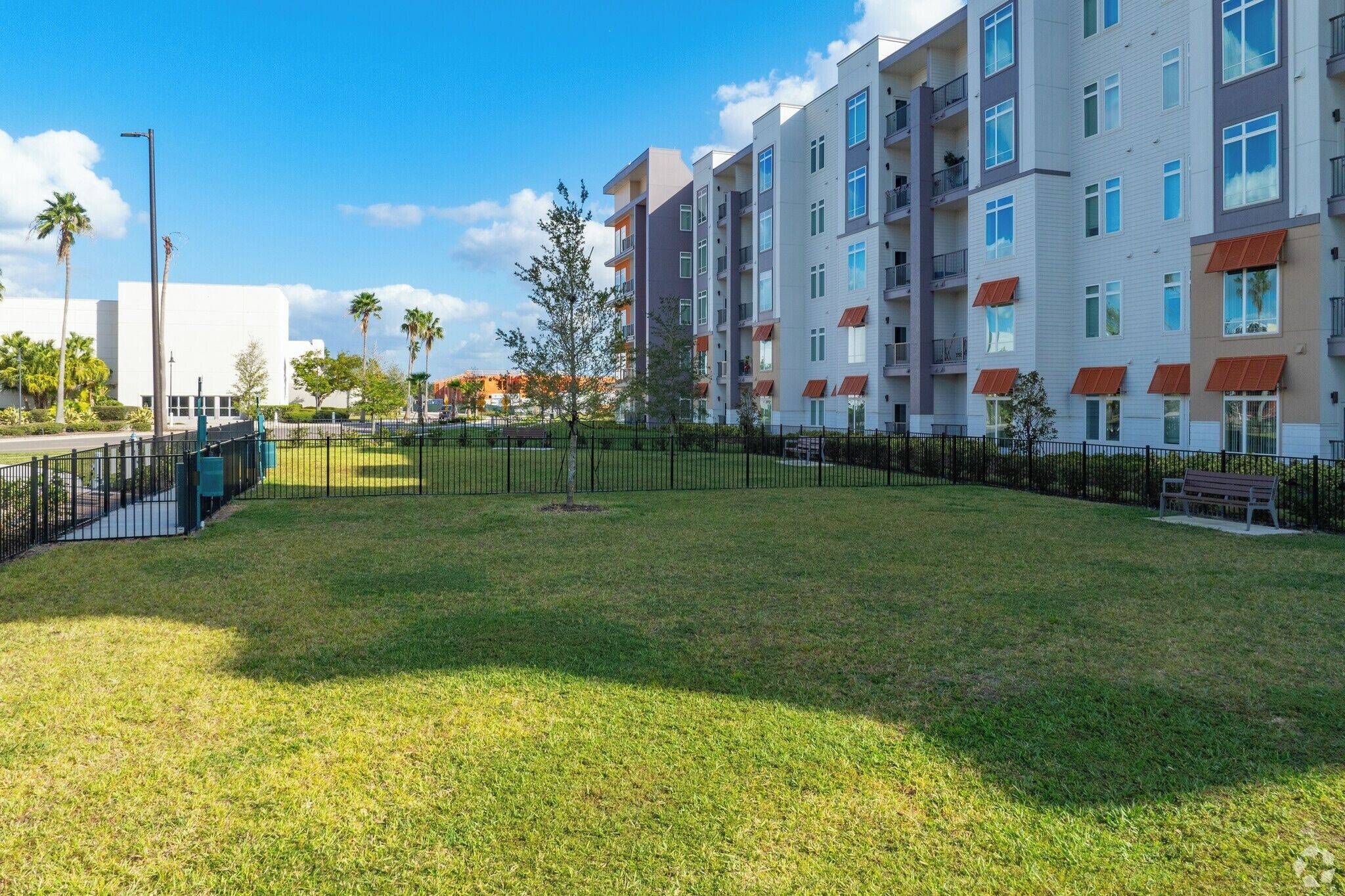 A multi-story residential building with balconies, a fenced courtyard, and a clear sky.