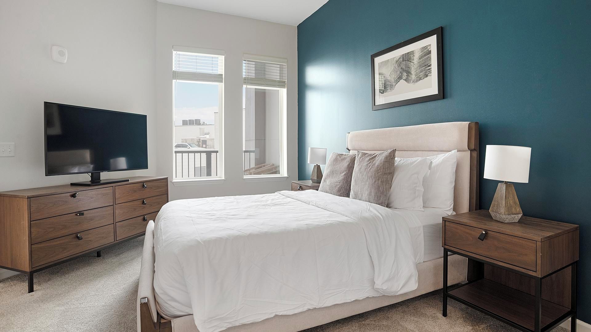 A bedroom with a bed, a TV, a nightstand, and a window with blinds.