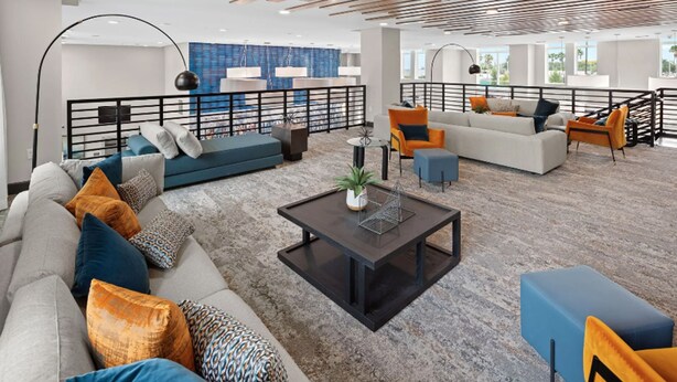 A spacious living area with a modern design, featuring a large sofa set, a coffee table, and a balcony with a railing. - Landing Orlando Universal (Orlando)