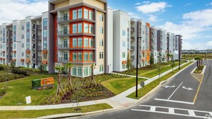 A multi-story residential building with balconies, a landscaped front yard, and a clear sky. - Landing Orlando Universal (Orlando)