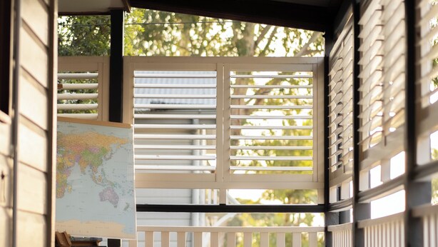A wooden deck with a white railing, a map on a stand, and a view of trees through the railing. - House of Fairy Wren - Fully renovated charming Queenslander! 10 Mins to BNE CBD! (Annerley)