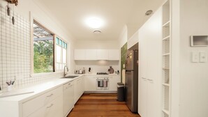 A modern kitchen with white cabinetry, a wooden floor, and a built-in oven. - House of Fairy Wren - Fully renovated charming Queenslander! 10 Mins to BNE CBD! (Annerley)