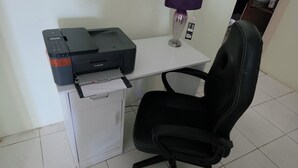 A printer on a desk with a chair, a small cabinet, and a purple lamp.