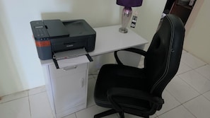 A printer on a desk with a chair, a small cabinet, and a purple lamp.
