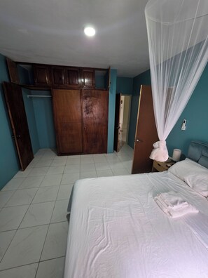 A hotel room with a bed, a wardrobe, a wardrobe mirror, a bedside table with a lamp, and a curtain.