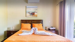 Ein ordentlich bezogenes Bett mit einer orangefarbenen Bettdecke und zwei weißes Handtücher, die als Herz auf dem Bett gefaltet sind.