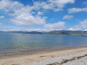 A beach with clear water, distant mountains, and a few boats.