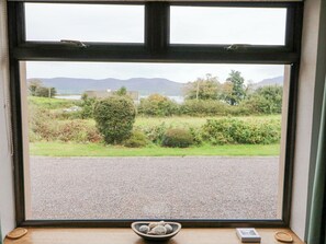 A window with a view of a gravel road, greenery, and distant mountains.