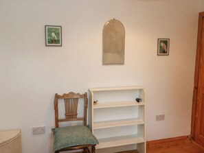 A room with a wooden chair, a white shelf unit, and two framed pictures on the wall.