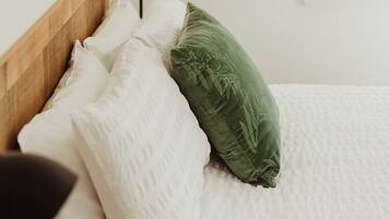 Un letto con una testiera in legno, biancheria da letto bianca e un cuscino verde.