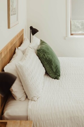 A bed with a wooden headboard, white bedding, and a green pillow.