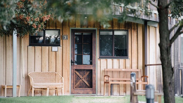 A wooden building with a large door, two windows, and two wicker chairs outside. - The Rosella - One-bedroom cottage at Bundaleera Vineyard (Relbia)