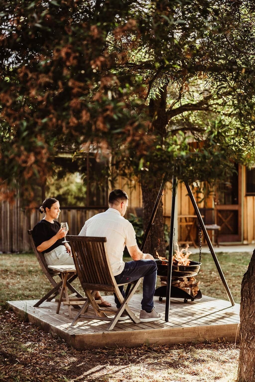 Un couple est assis sur un banc en bois à l’extérieur, avec un foyer au centre.