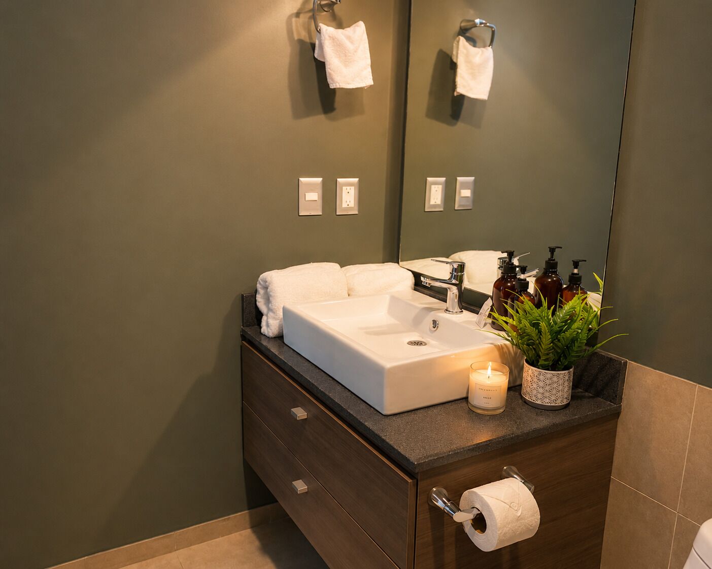 Un bagno moderno con lavandino bianco, uno specchio, un porta asciugamani, una pianta e una candela.