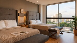 Una habitación de hotel moderna con dos camas, un ventanal con vistas a la ciudad, una mesita de noche con lámpara y una planta en maceta.