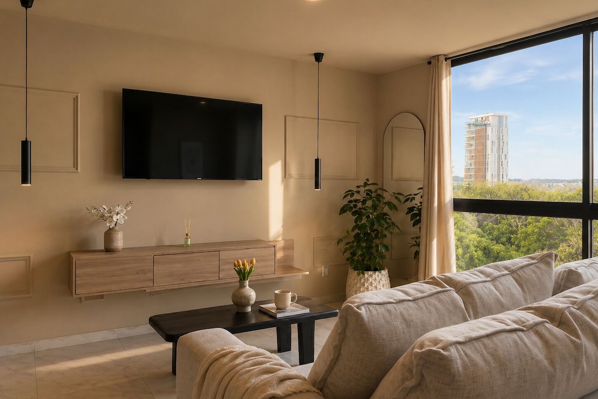 Una sala de estar moderna con un televisor grande, una consola de madera, una mesa de centro, un sofá y un ventanal con vistas a edificios y árboles.
