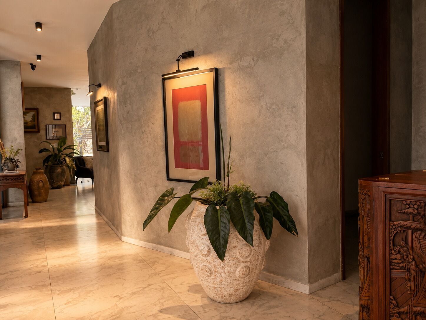 A hallway with a large potted plant, a framed artwork on the wall, and a wooden cabinet.