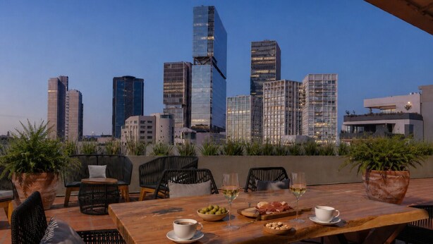 Una terraza en la azotea con vistas a un horizonte urbano, una mesa de madera con sillas y plantas en macetas.